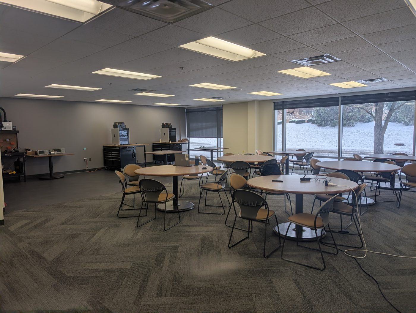 Round tables with chairs for team work, in front of floor-to-ceiling windows looking out on a snowy lawn.
